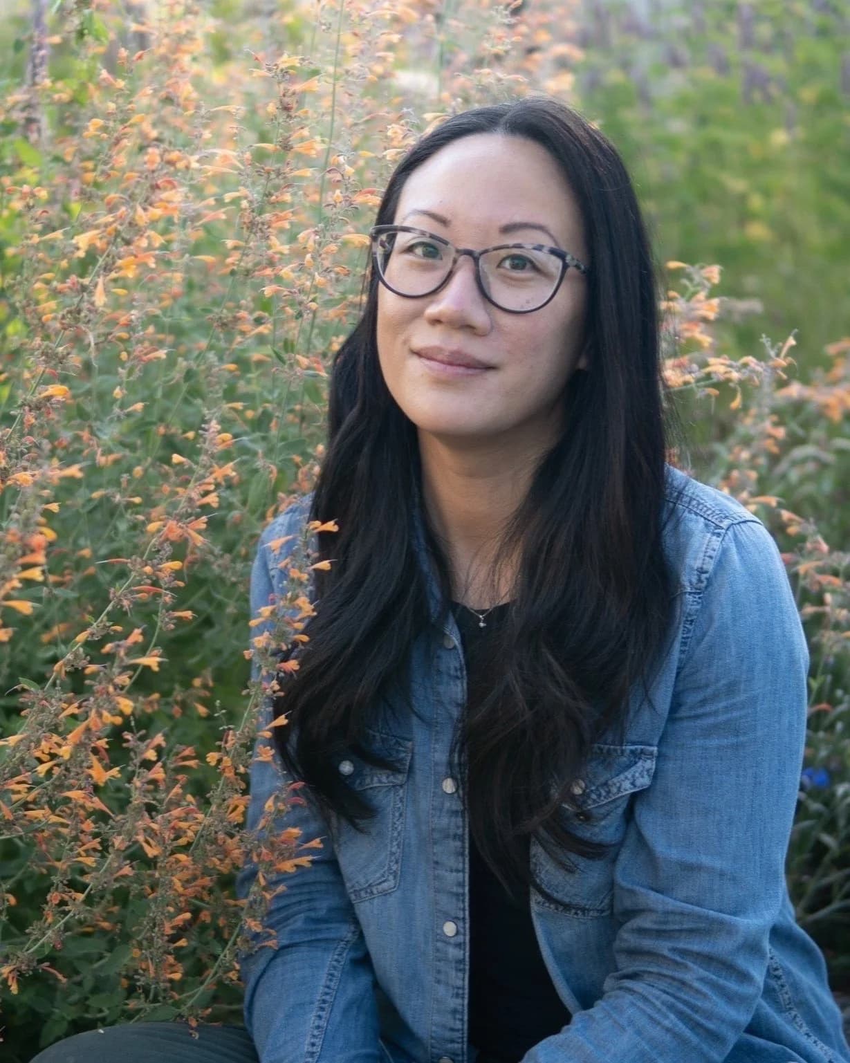 Chris Chung, seated outdoors in a denim shirt among flowering agastache.
